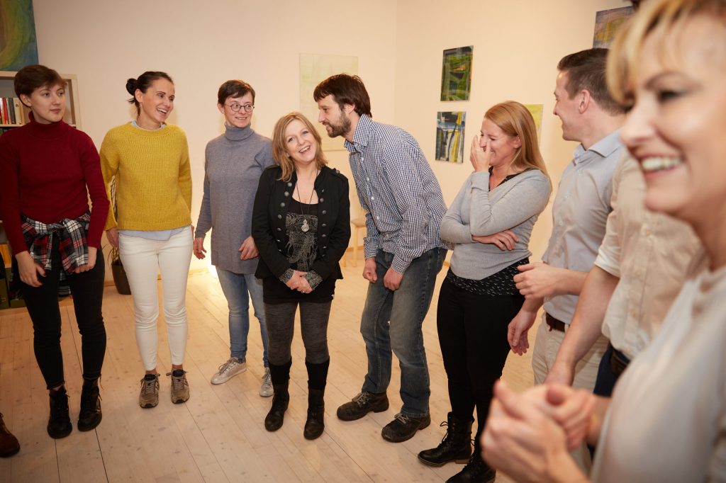 Group of adults standing in a circle indoors, smiling and chatting during a casual gathering.