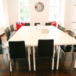 seminarraum-mieten-raum1-meeting-raum-2 - Zentrum für Stimme & Sprechen Bright conference room with a long white table, black chairs, and a colorful circular clock on the wall.